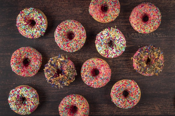 Different donuts arranged with colorful sprinkles on rustic wooden table