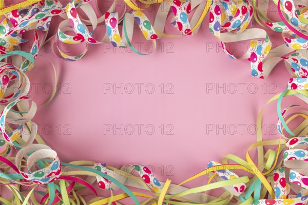 Colourful streamers form a frame on a pink background, Mardi Gras