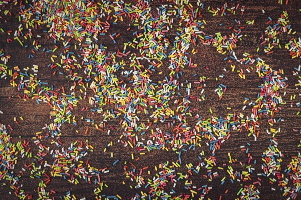Colourful sprinkles scattered on dark wooden table