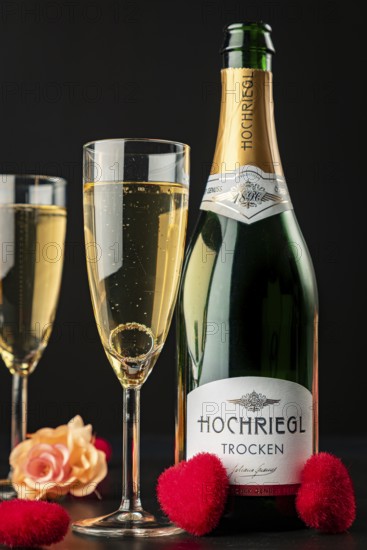 Bottle and glasses with sparkling wine, with roses, hearts and ring in glass on black background