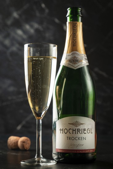 A champagne bottle next to a glass with sparkling contents, cork in the background