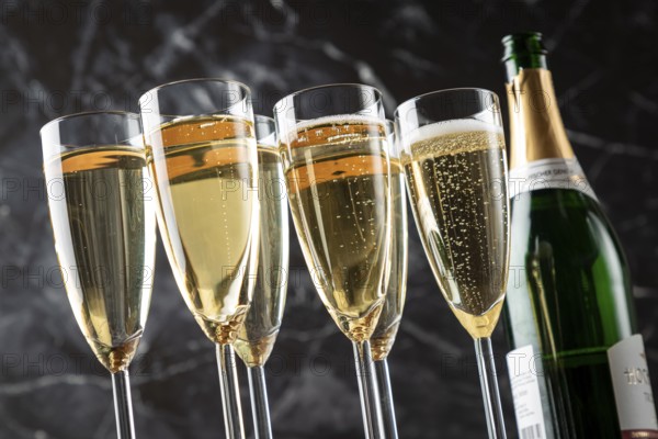 Six glasses filled with sparkling wine and an open champagne bottle against a black background