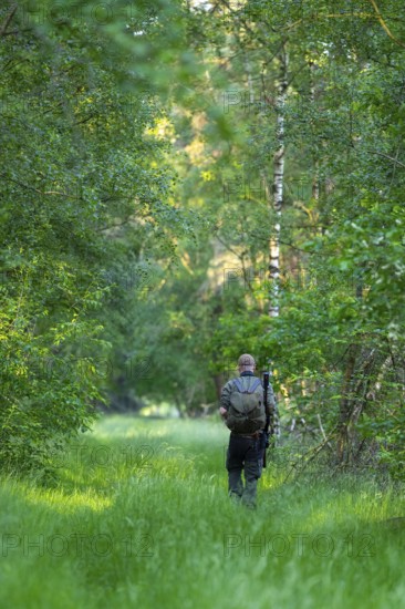 Hunter with backpack and gun goes to the residence, Ahlhorn, Lower Saxony, Germany