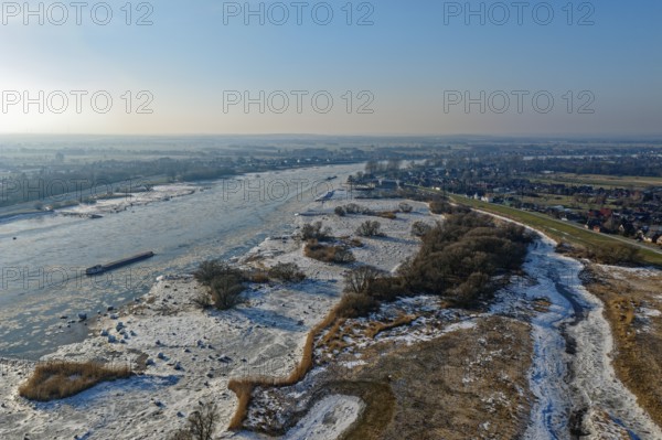 On a cold winter day, a barge sails downstream on the Elbe near Hamburg when there is slight ice. The foothills of the Elbe are icy in the flooded area. Kirchwerder, Hamburg, Germany