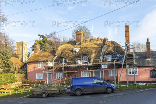 Thatcher at work replacing thatch ridge of thatched country pub building, Sorrel Horse, Shottisham, Suffolk, England, UK