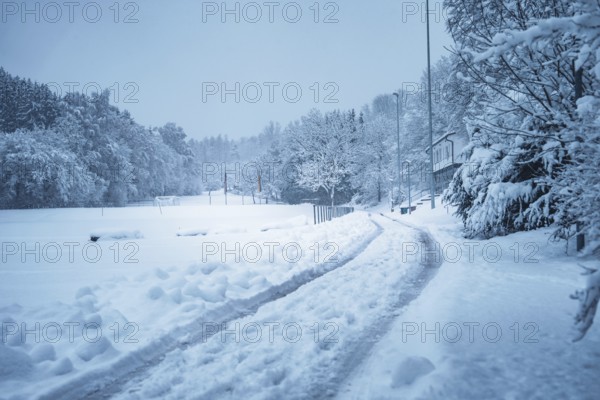 A snowy road leads through a wintry landscape with trees and houses, Besenfeld, Black Forest, Germany