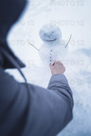 A person builds a small snowman surrounded by snow, broom field, Black Forest, Germany