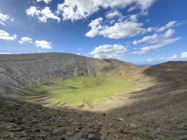 View of the Caldera Blanca volcano cauldron against blue sky with white clouds, Mancha Blanca, Lanzarote, Canary Islands, Spain