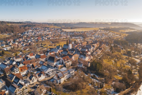 Aerial view of a town with a central church surrounded by red roofs and winter landscape under blue sky, Dornstetten, Freudenstadt district, Germany