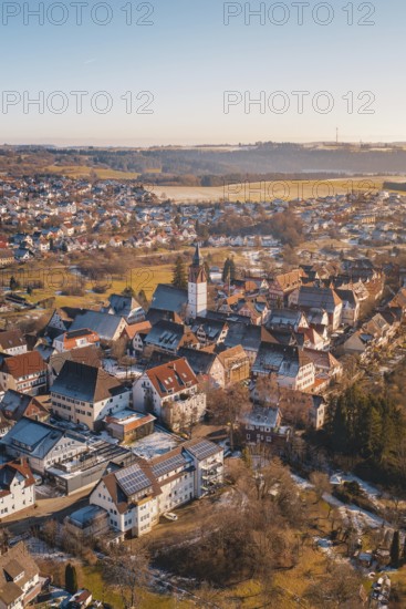 Aerial view of a town with church in the center, surrounded by buildings and winter landscape under blue sky and sunshine, Dornstetten, Freudenstadt district, Germany