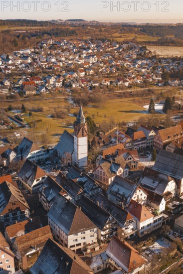 Aerial view focusing on church surrounded by city buildings in a wintry environment in sunlight, Dornstetten, Freudenstadt district, Germany