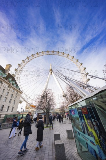 People walk under a big Ferris wheel on a sunny day, London Eye, London, United Kingdom