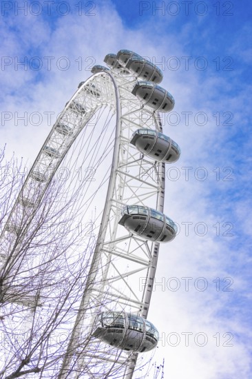 A large Ferris wheel juts into the blue sky surrounded by clouds, London Eye, London, United Kingdom