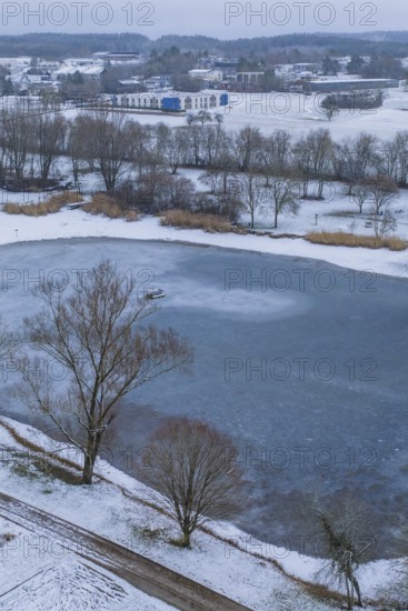 Small lake surrounded by snow-covered park and village in the background, icy surface, Empfingen, Freudenstadt district, Germany