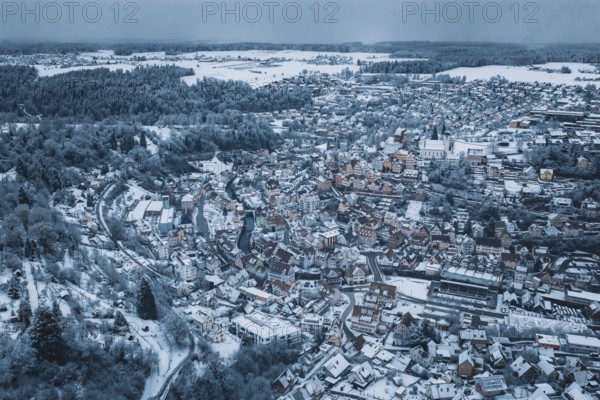Snowy city seen from the air with numerous houses and snow-covered roofs, surrounded by forests and hills in a wintry atmosphere, Altensteig, Calw district, Germany