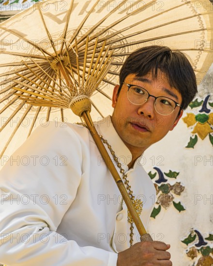 Young man wearing a parasol in traditional clothing presents himself for the photographers, Wat Arun Buddhist temple, Bangkok, Thailand's metropolis, Thailand