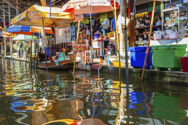 Wooden boat and umbrellas are reflected on the Damneon Saduak floating market channel near Bangkok, Ratchaburi District, Thailand