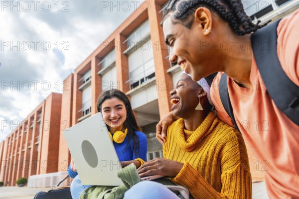 Group of diverse university students enjoying a moment of laughter while using a laptop together on campus, representing friendship, collaboration, and modern education