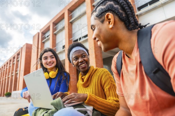 Diverse group of university students collaborating and smiling around a laptop outdoors on campus, sharing ideas, studying and enjoying casual teamwork and friendship in daylight