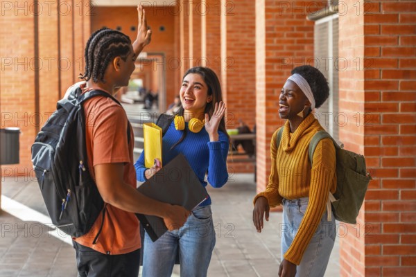 Group of diverse university students on campus, one male and two females, standing in a brick corridor, smiling and high fiving, representing education and friendship
