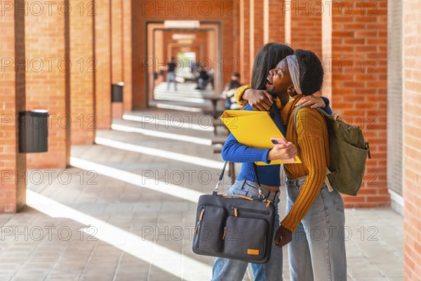 Joyful multiracial students are sharing a warm hug on a university campus, celebrating their reunion and bond in an educational setting with building columns and other students in the background
