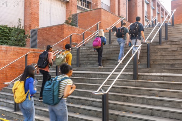 Diverse group of university students climbing outdoor campus stairs with backpacks, heading toward a brick academic building, symbolizing learning, ambition and teamwork