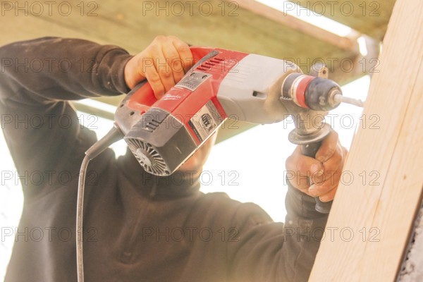 A worker uses a drill on vertical wooden surfaces, carpentry construction site, roof extension, renovation, Stuttgart, Germany