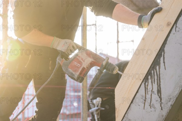 Worker with drill in sunlight working on wood on construction site, carpentry construction, roof extension, renovation, Stuttgart, Germany