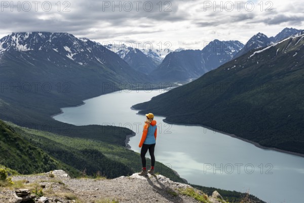 Female mountaineer enjoying views of blue lake and mountains on Twin Peaks Trail, Eklutna Lake, Chugach Mountains, Chugach State Park, Alaska, USA