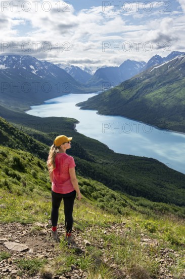 Female mountaineer enjoying views of blue lake and mountains on Twin Peaks Trail, Eklutna Lake, Chugach Mountains, Chugach State Park, Alaska, USA