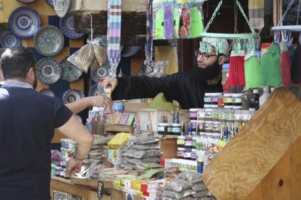 Cosmetics seller at a lively market in Fez, surrounded by goods and buyers, Fez, Morocco