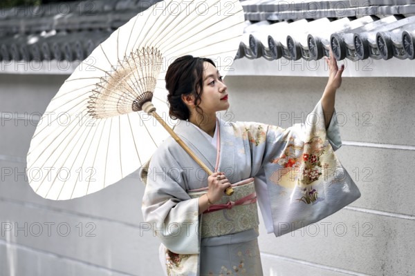 Woman wearing kimono with umbrella gesturing in front of a wall, Kyoto, Higashiyama, Japan
