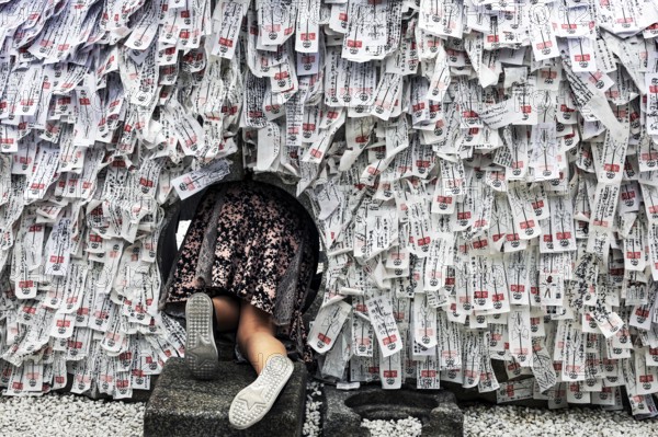 Person crawling through hole in stone with strips of paper in Yasui Konpiragu Temple, Kyoto, Gion, Japan