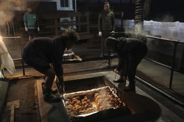 Preparing a traditional hangi in a pit with steam and people in Rotorua, Rotorua, Bay of Plenty, New Zealand