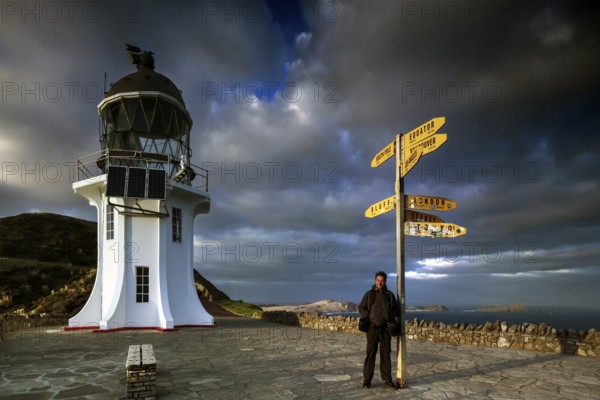 Lighthouse and yellow signpost at Cape Reinga under dramatic sky, Cape Reinga, Northland, New Zealand
