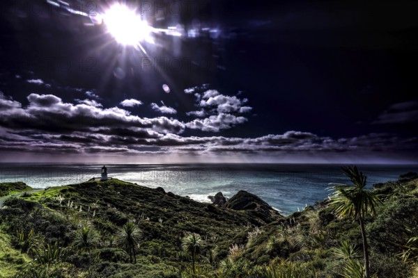 Cape with lighthouse and Pohutukawa trees under bright sky in Cape Reinga, Cape Reinga, New Zealand
