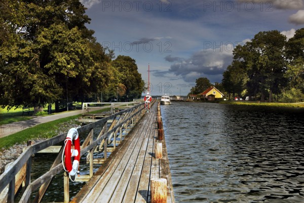Long wooden walkway along the Göta Canal in a mountain, lined with trees and water under a cloudy sky, mountain, Sweden