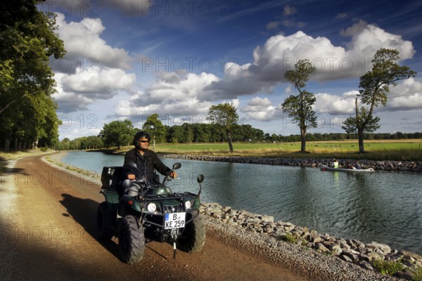 Person on an ATV rides along the Göta Canal in Borensberg under a blue sky, Borensberg, Sweden