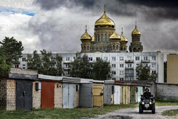 In front of an imposing church, golden domes rise above prefabricated buildings and garages, Liepaja, Karosta, Latvia