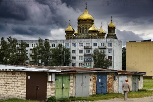 Prefabricated building in front of cathedral with golden domes and garages under dramatic sky, Liepaja, Karosta, Latvia