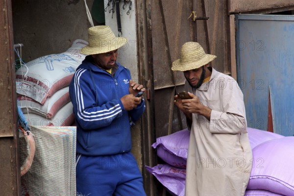 Two men in traditional hats are talking relaxed at a market in Achaouikh, Achaouikh, Morocco