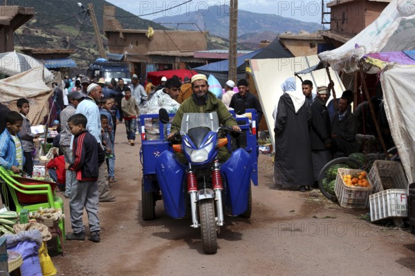 Busy market day in Achaouikh with people, vehicles and stalls, zero