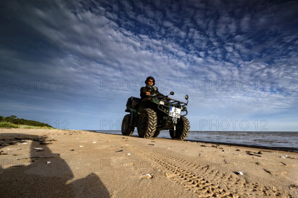 Person riding on ATV along the beach under a cloudy sky, Kolka, Latvia