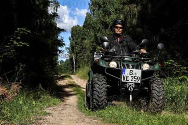 Man rides ATV on a forest trail surrounded by tall vegetation, Ligatne, Gauja National Park, Latvia