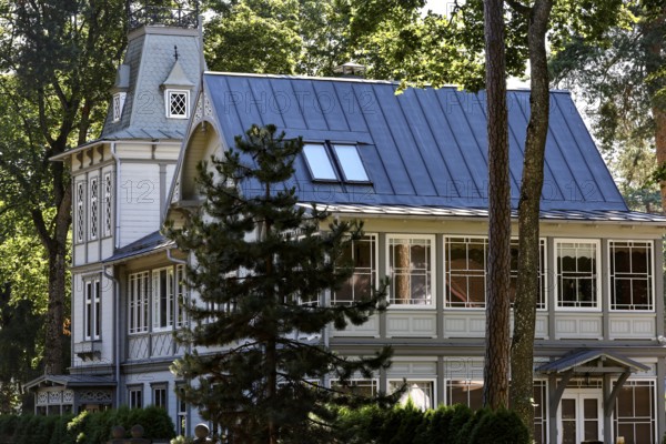 Elegant art nouveau wooden house with eye-catching blue roof under tall trees, Majori, Jurmala, Latvia