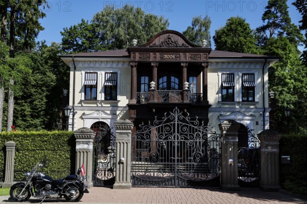Large wooden house with ornate gate and parked motorcycle in front of it, Jurmala, Latvia