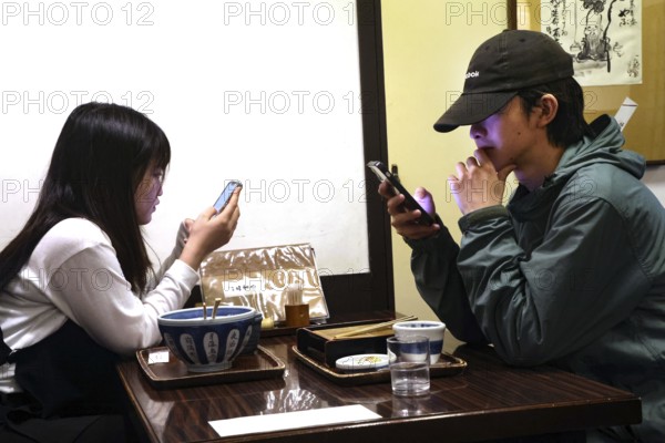 A couple is sitting in a restaurant in Kurashiki, both engrossed in their smartphones, Kurashiki, Japan