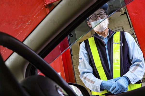 Worker wearing mask and safety vest serves customers through a car window, Kobe, Hyogo, Japan