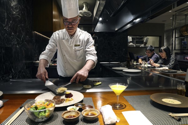 Chef prepares teppanyaki dish in front of guests at Kobe Plaisir restaurant, Kobe, Hyogo, Japan