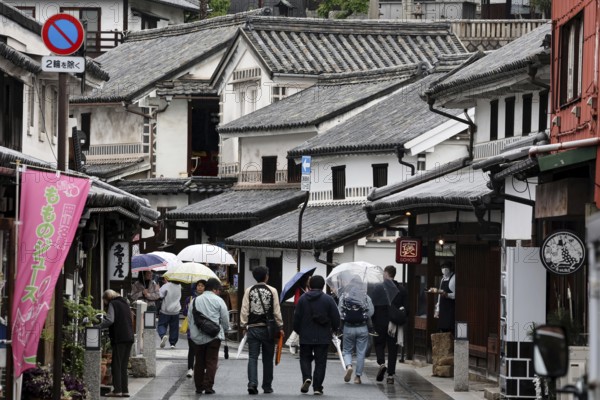 People with umbrellas walk through a historic street with traditional buildings in Kurashiki, Kurashiki, Okayama, Japan